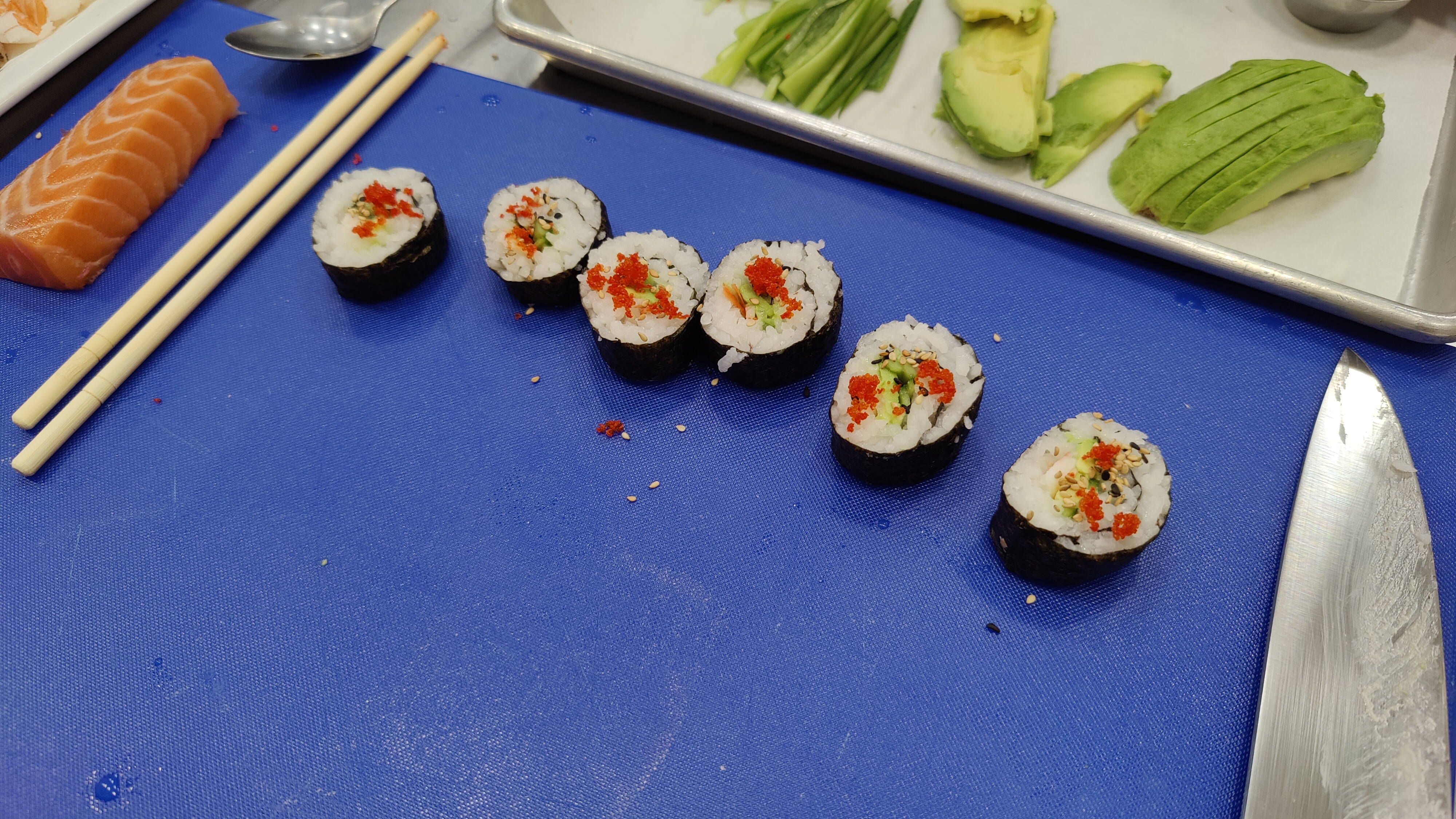 Six maki sit on the cutting board. There are toasted sesame seeds and roe on top. They are delicious.